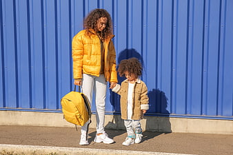 Mother and Child Walking with Yellow Backpack Against Blue Wall