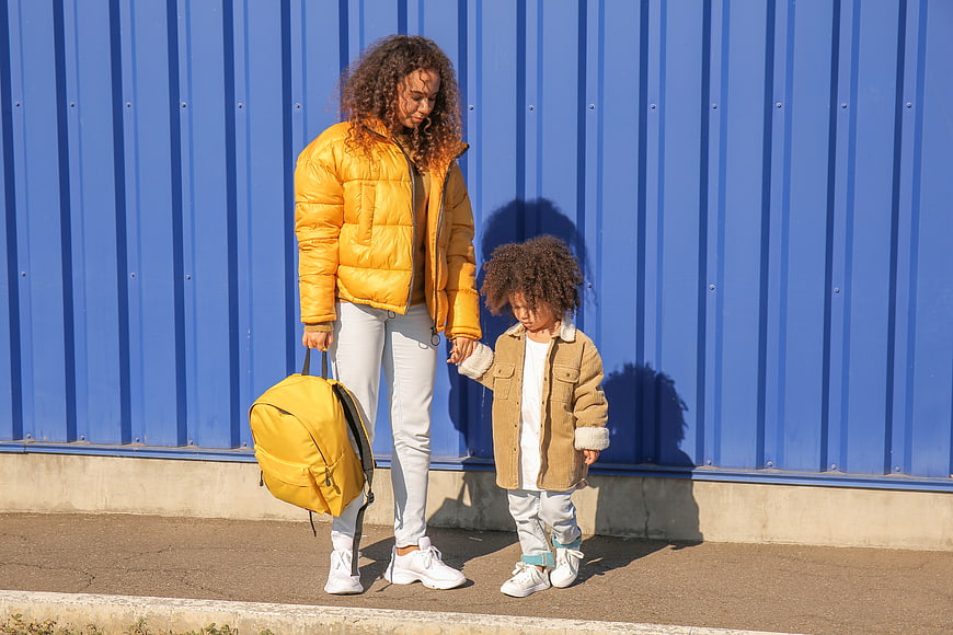 Mother and Child Walking with Yellow Backpack Against Blue Wall