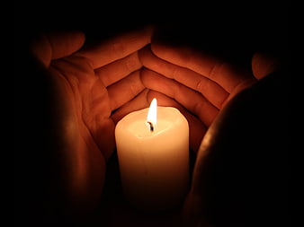 Hands cupping a lit candle in the dark