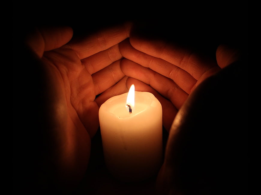 Hands cupping a lit candle in the dark