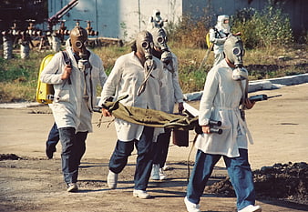 Rescue team in gas masks carrying stretcher during chemical disaster drill