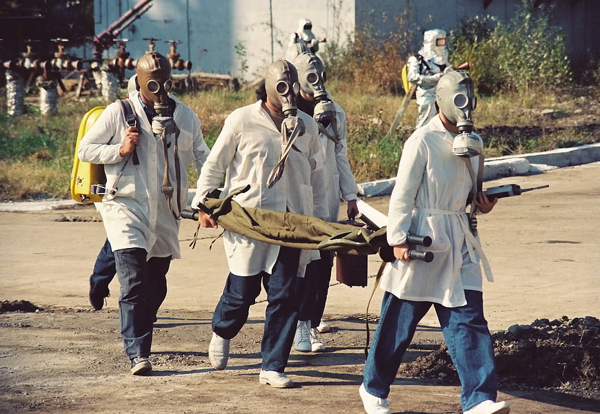 Rescue team in gas masks carrying stretcher during chemical disaster drill