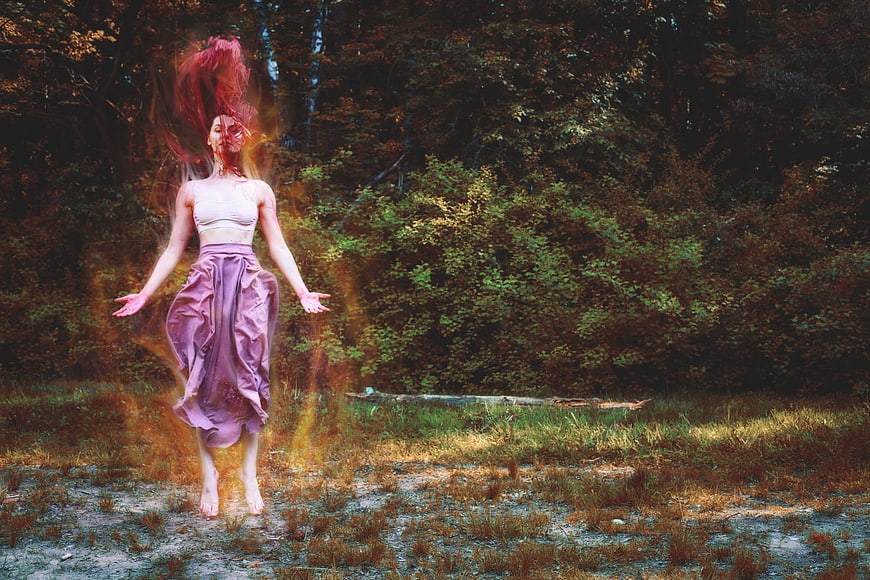 Mystical woman jumping in forest with fire effects