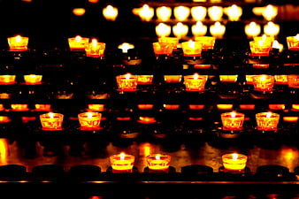 Rows of glowing votive candles in a dark church setting