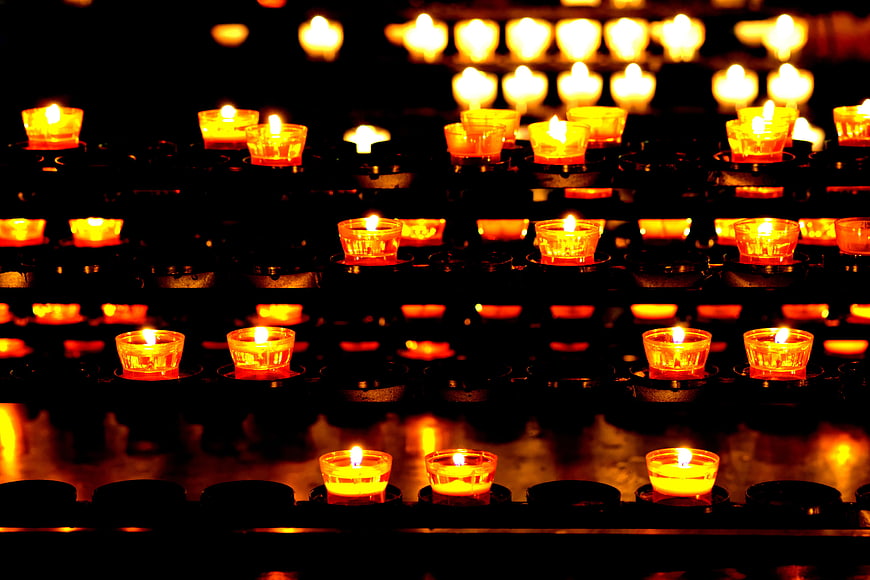 Rows of glowing votive candles in a dark church setting