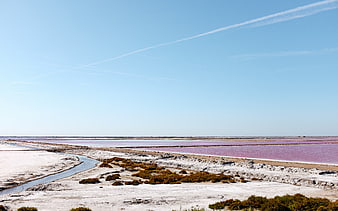 Pink salt flats landscape with blue sky and contrails