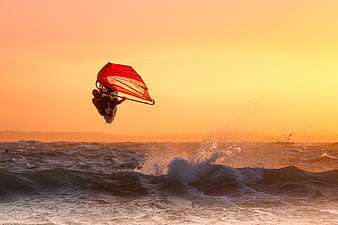 Windsurfer Jumping High Over Ocean Waves at Golden Sunset