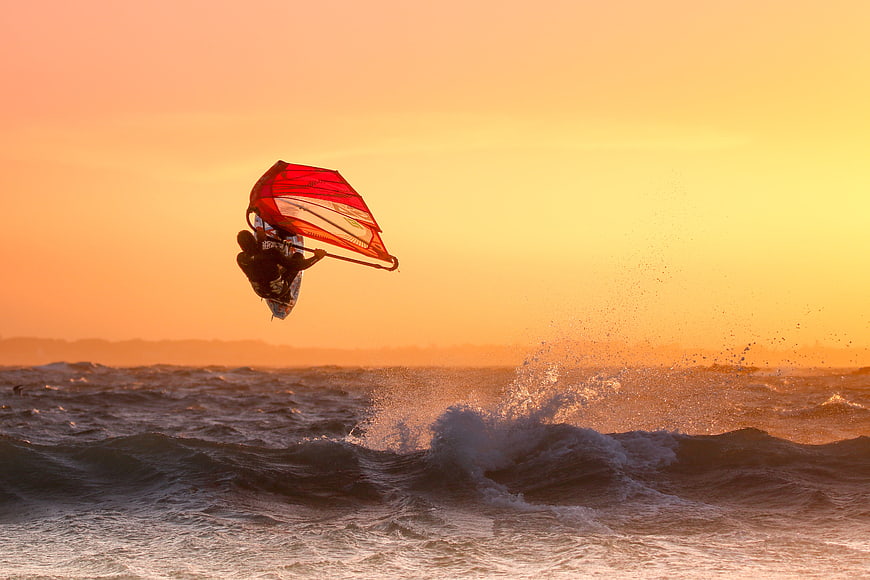 Windsurfer Jumping High Over Ocean Waves at Golden Sunset