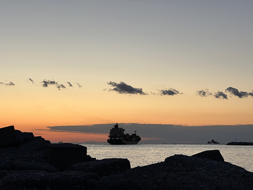 Cargo ship silhouette on ocean horizon at sunset