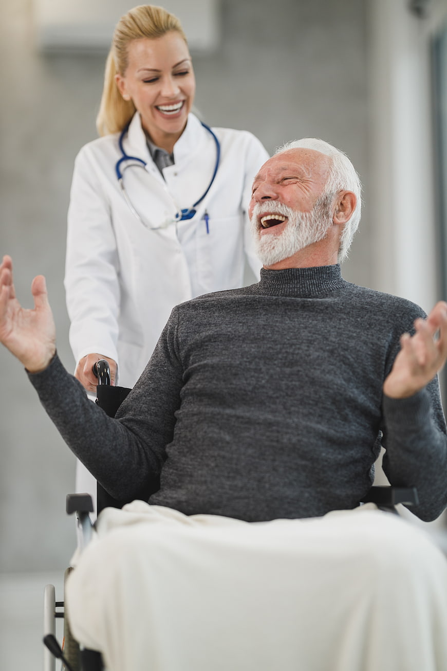 Happy Senior Man in Wheelchair Laughing with Female Doctor