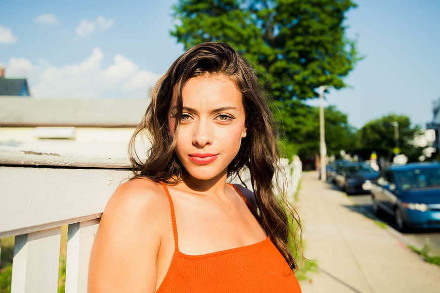 Portrait of young woman in orange top leaning on white fence outdoors