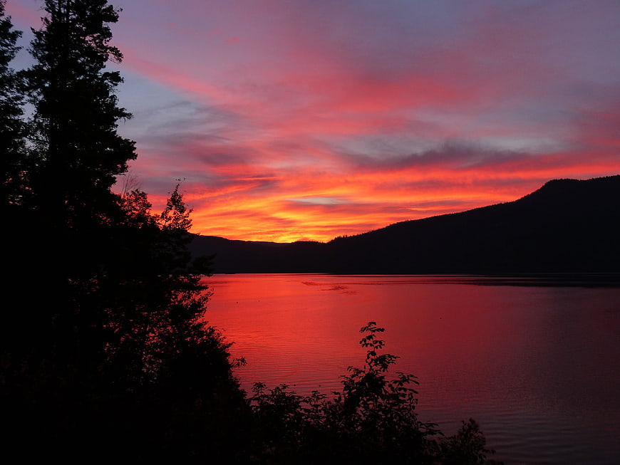 Vibrant red sunset over lake with silhouetted mountains