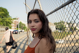 Portrait of young woman with dark hair by chain link fence