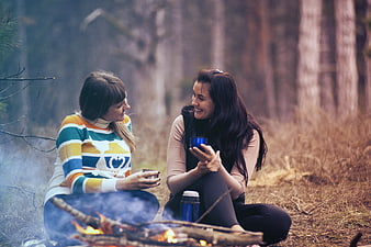 Two happy women laughing by a campfire in the forest