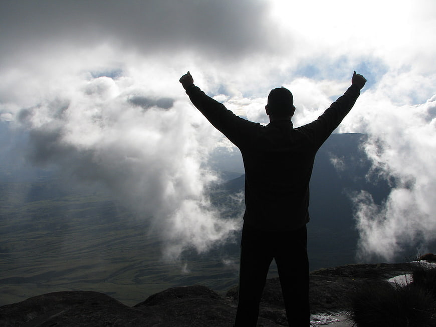 Silhouette of Man Celebrating on Mountain Peak Above Clouds