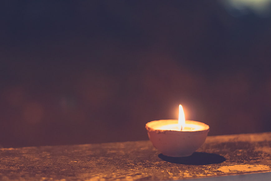 Small lit diya oil lamp on textured wooden surface