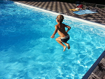Young boy jumping into a blue swimming pool