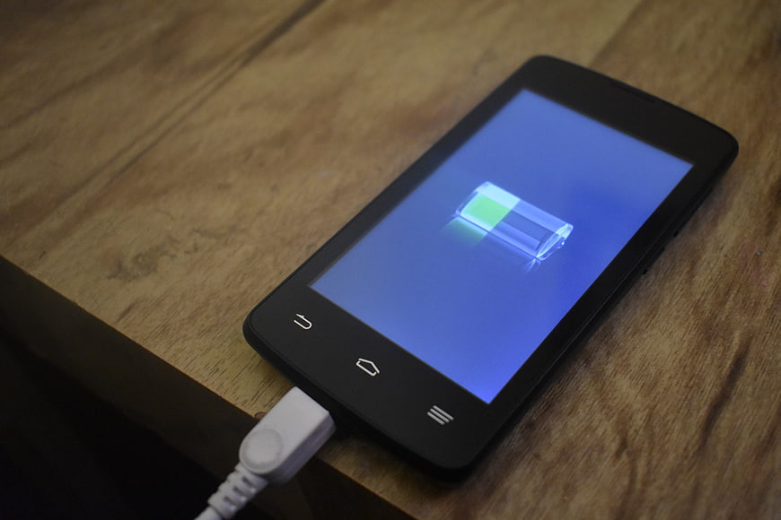 Black Android smartphone charging on wooden table with battery icon