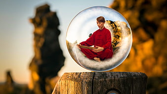 Woman meditating in red robe inside a glass sphere on a wooden post