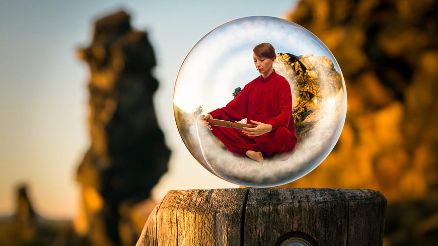 Woman meditating in red robe inside a glass sphere on a wooden post