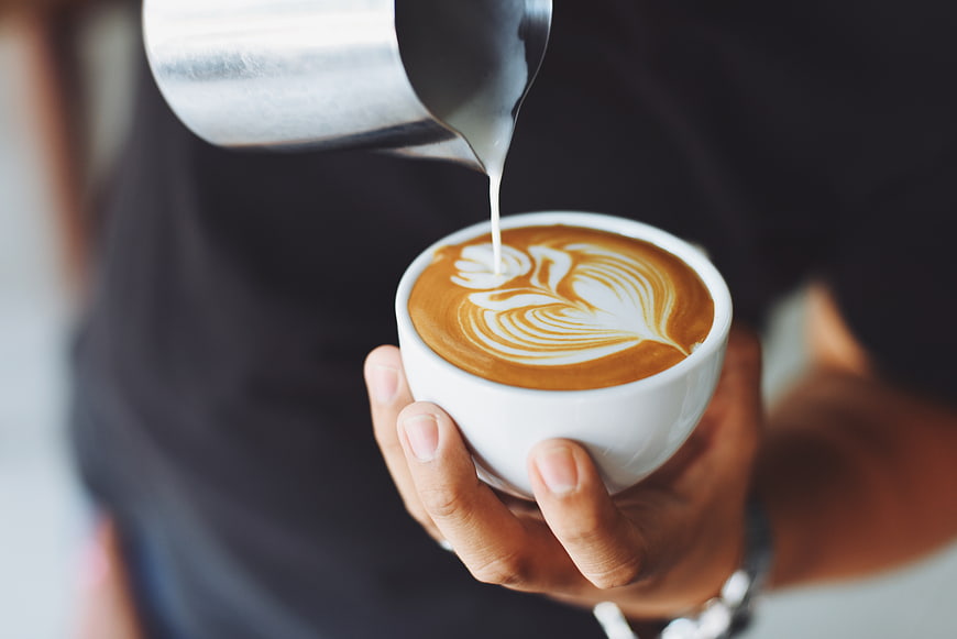 Barista pouring latte art into a white coffee cup