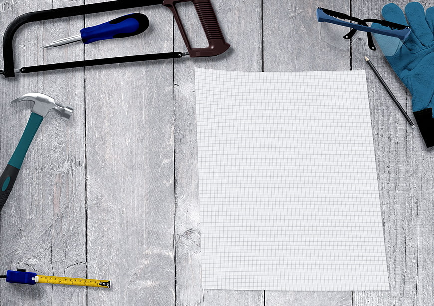 Flat lay of carpentry tools and graph paper on white wooden table