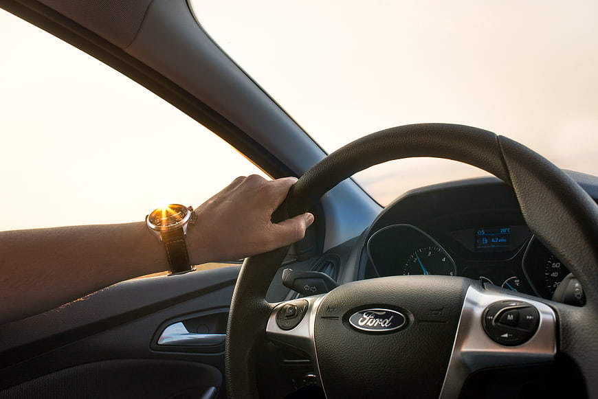 Man's Hand on Steering Wheel Driving Car at Sunset