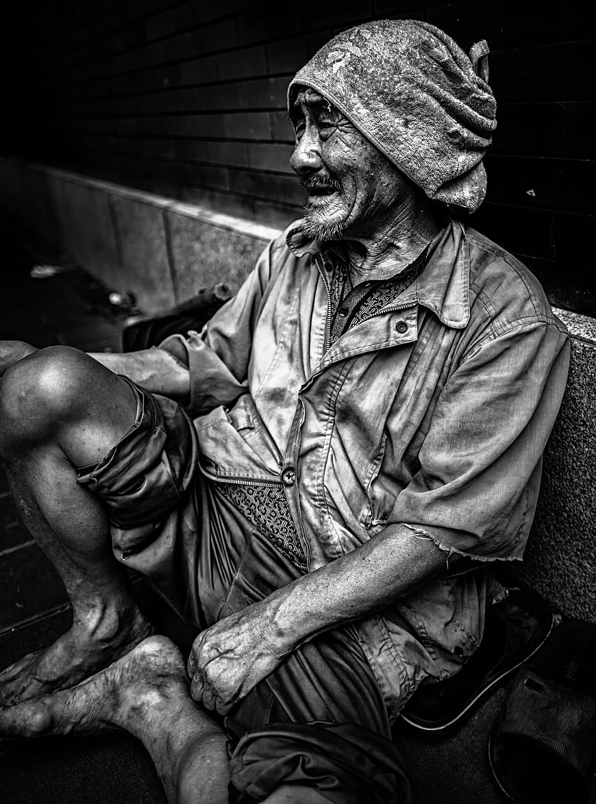 Black and white portrait of an elderly homeless man sitting on a bench