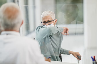 Senior woman coughing into elbow at medical clinic