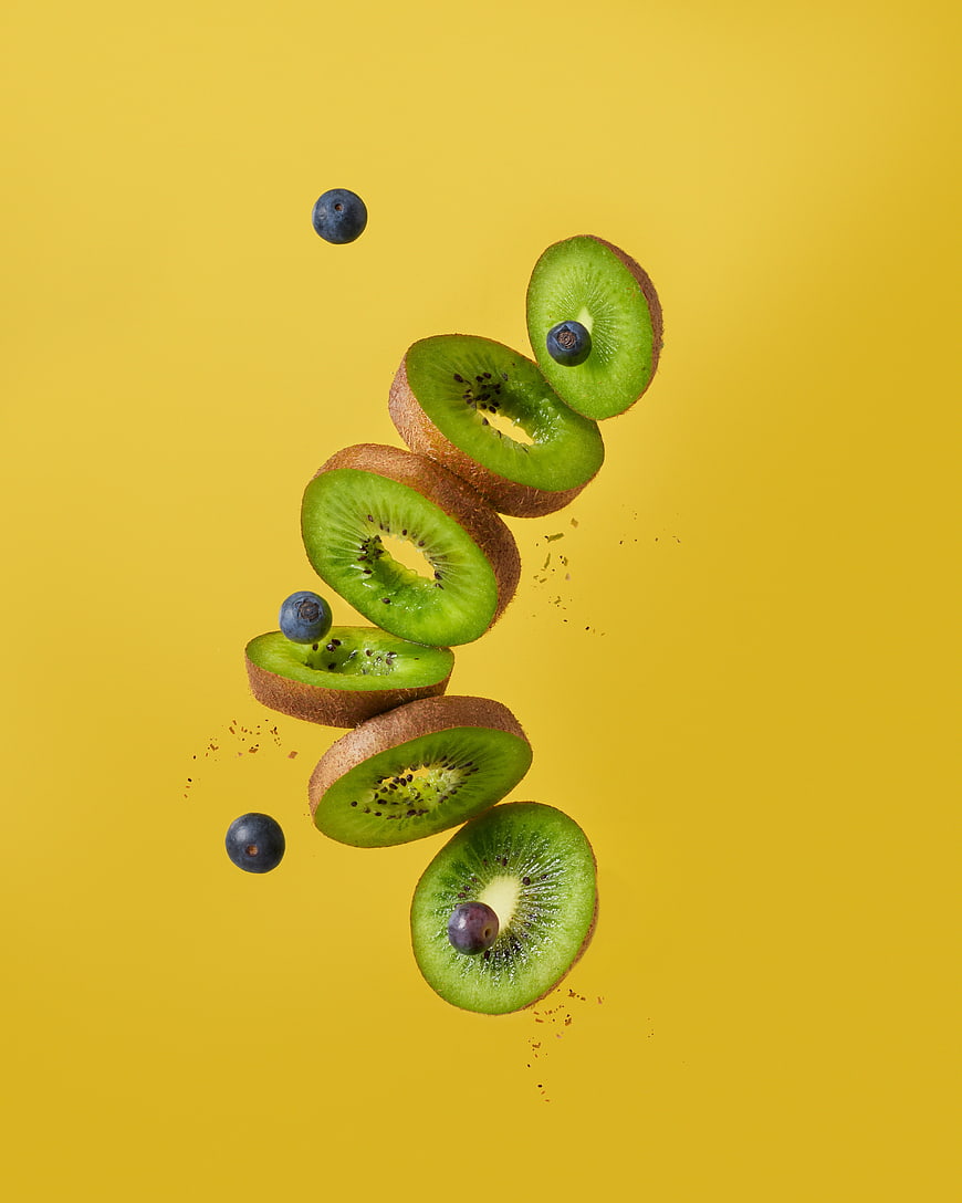 Floating kiwi slices and blueberries on yellow background