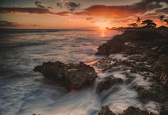Dramatic Sunset Over Rocky Coastline with Silhouetted Palms