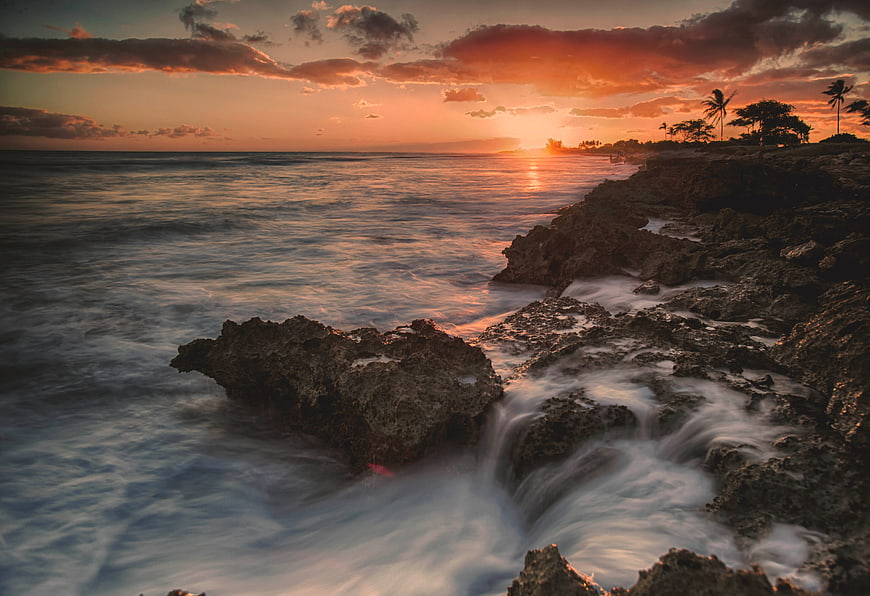 Dramatic Sunset Over Rocky Coastline with Silhouetted Palms