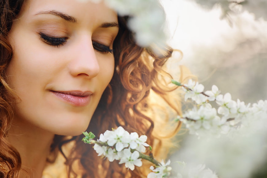 Close-up of woman with curly hair smelling white spring blossoms