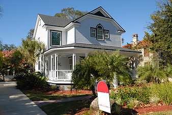 White two-story house with porch and for sale sign