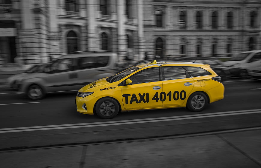 Yellow taxi driving on city street with motion blur