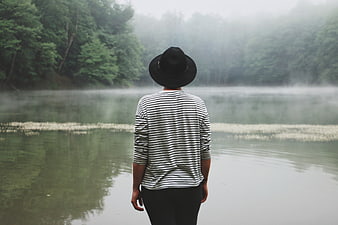 Man in Striped Shirt and Hat Standing by Misty Lake