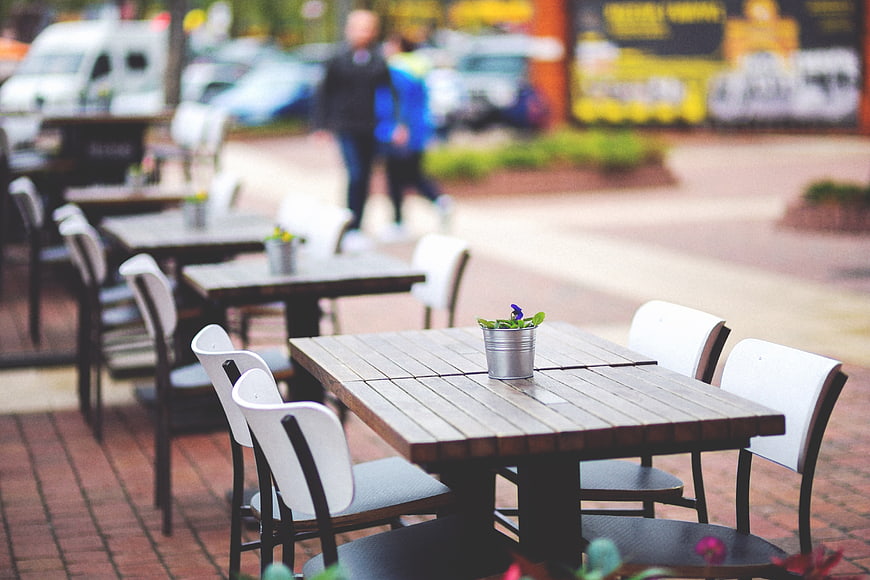 Empty Outdoor Cafe Tables With White Chairs On Brick Pavement