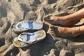 Woman's bare feet and flip-flops on sandy beach