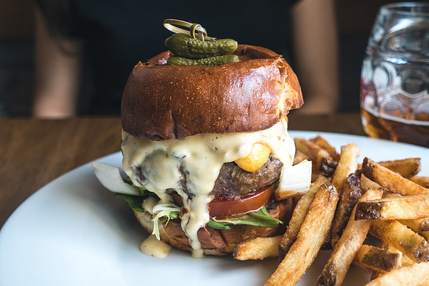 Gourmet Burger with Pickles and Fries on White Plate