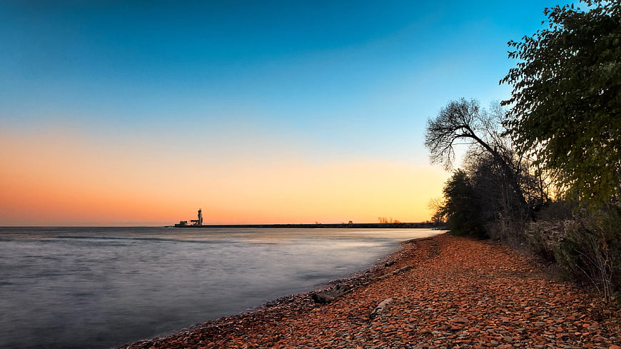 Serene Autumn Shoreline with Lighthouse at Sunset