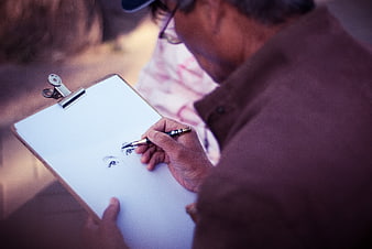 Senior man sketching eyes on clipboard outdoors