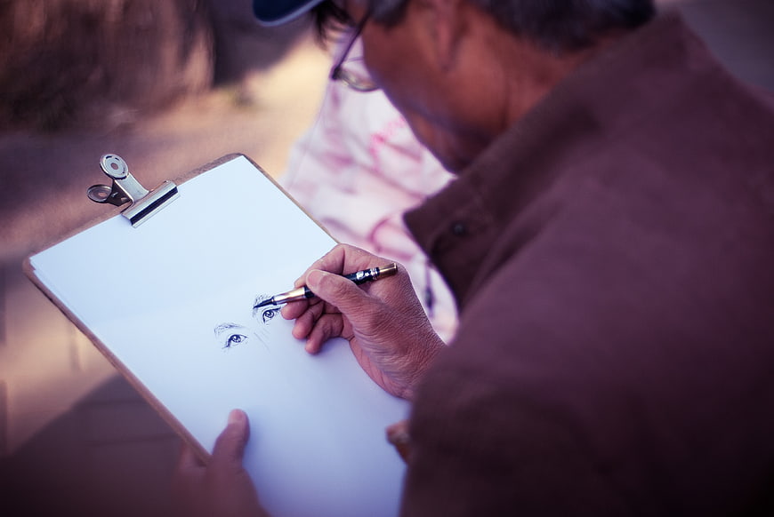 Senior man sketching eyes on clipboard outdoors