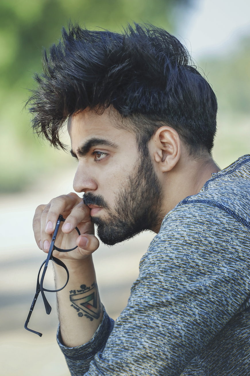 Thoughtful Young Man with Beard Holding Glasses Outdoors