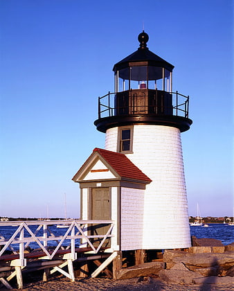 White and Black Lighthouse on Rocky Shore by Sea