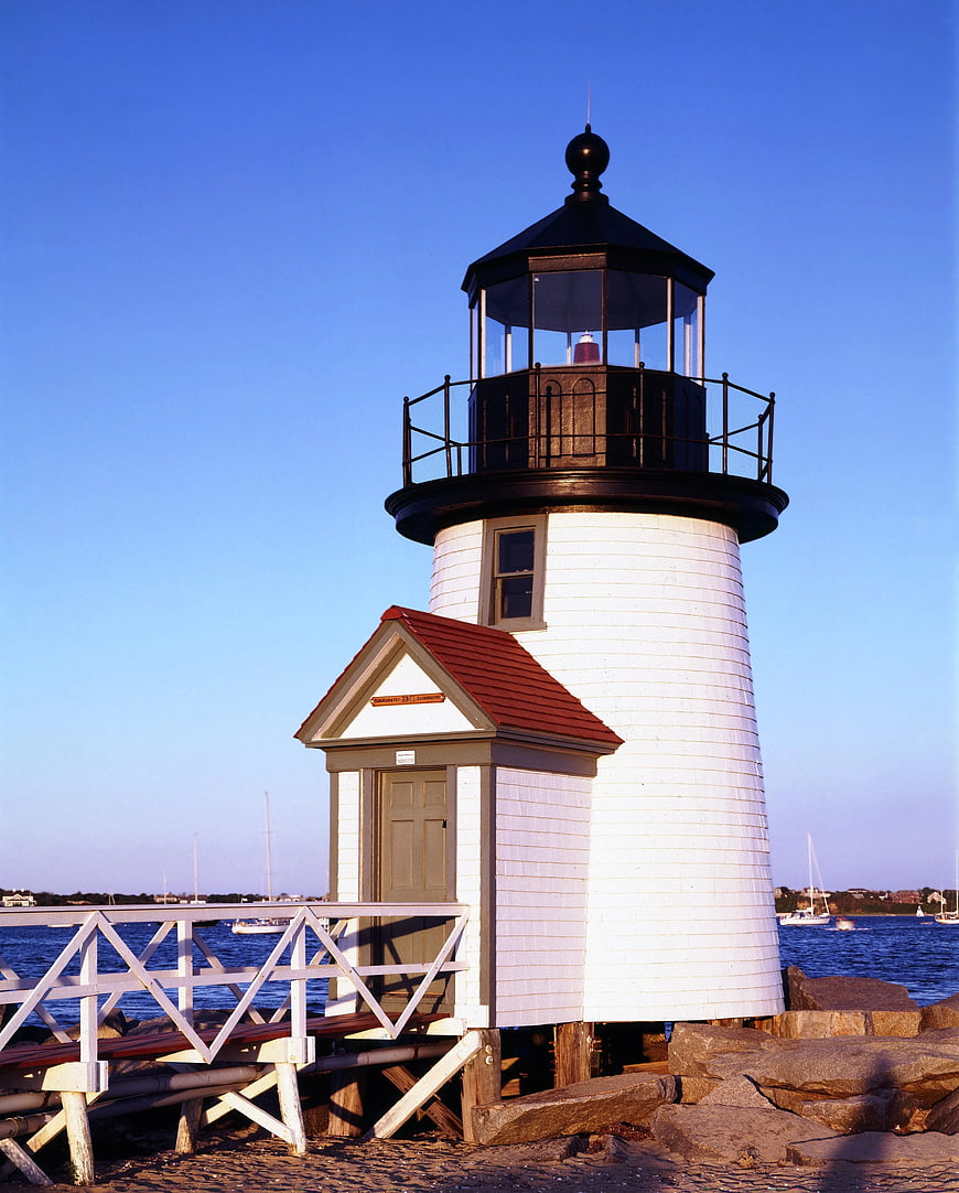 White and Black Lighthouse on Rocky Shore by Sea