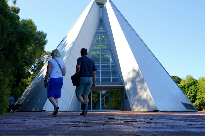 Couple walking toward modern pyramid building in botanical garden