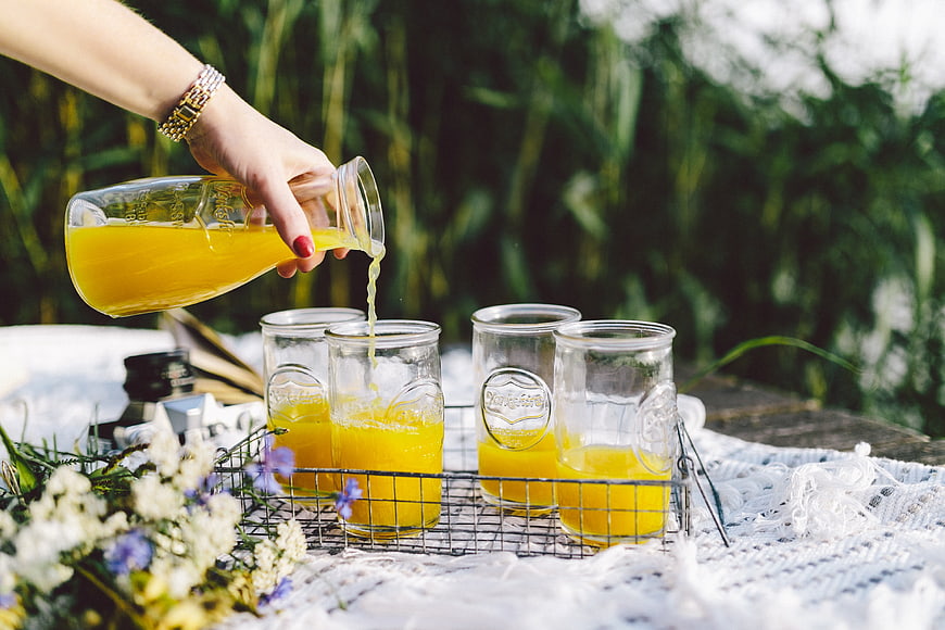 Pouring Fresh Orange Juice into Mason Jars at Summer Picnic