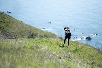 Woman standing on grassy cliff overlooking ocean