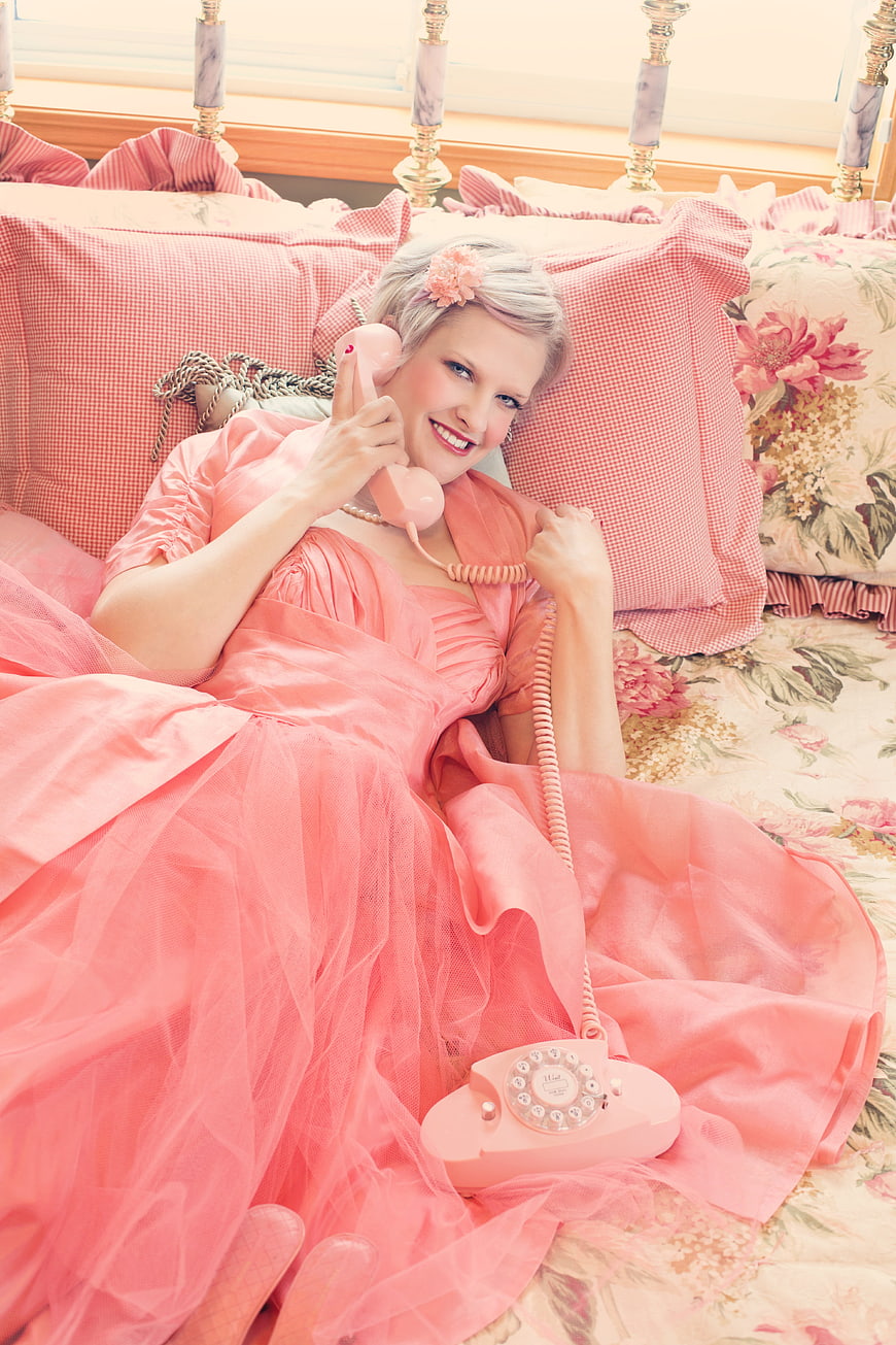 Vintage Woman in Pink Gown Talking on Retro Rotary Phone in Bed