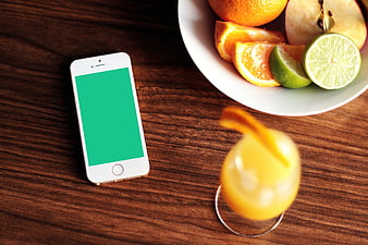 Smartphone with green screen next to fruit bowl and juice